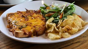 Ein Teller mit einem Steak, überzogen mit geschmolzenem Käse, dazu ein gemischter Salat und Kartoffelchips.