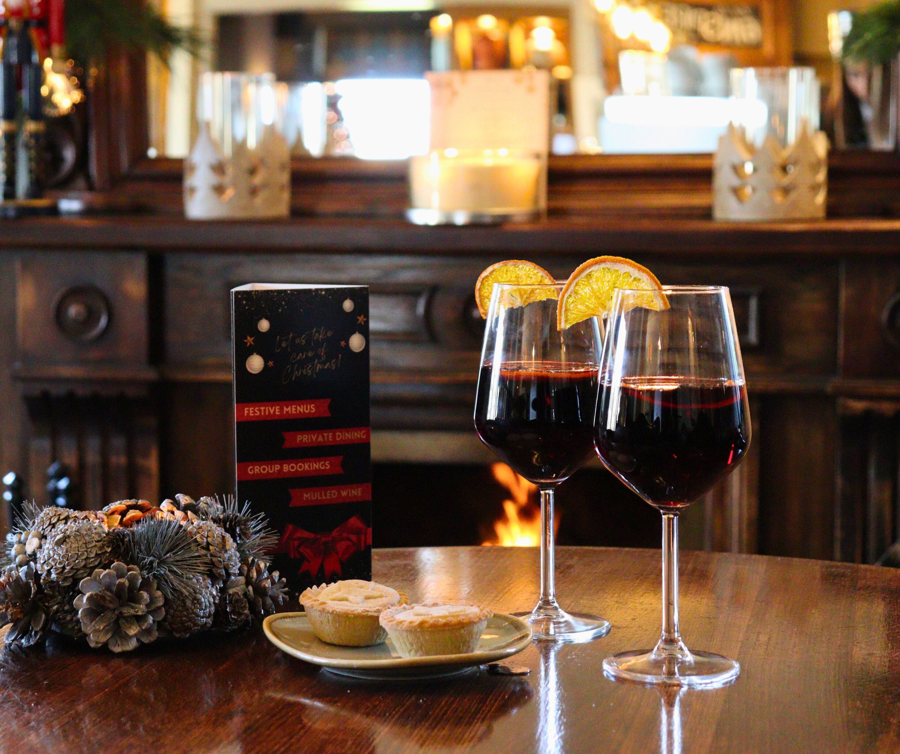 Zona de bar con dos copas de vino tinto, un plato de pasteles y un tablero de menú festivo.