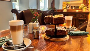 A dining table with a three-tiered cake, a mug of coffee, and a glass of milk. - The Gateway Hotel (Kendal)