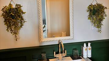 Un baño con un lavamanos blanco, armarios verdes, dos luces empotradas en la pared y dos plantas colgantes.