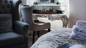 A room with a tufted sofa, a chair, a dresser with a mirror, and a window with curtains. - The Gateway Hotel (Kendal)
