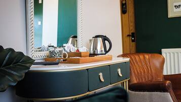 A room with a dark green wall, a white-framed mirror, a wooden cabinet with drawers, a brown leather chair, and a radiator.