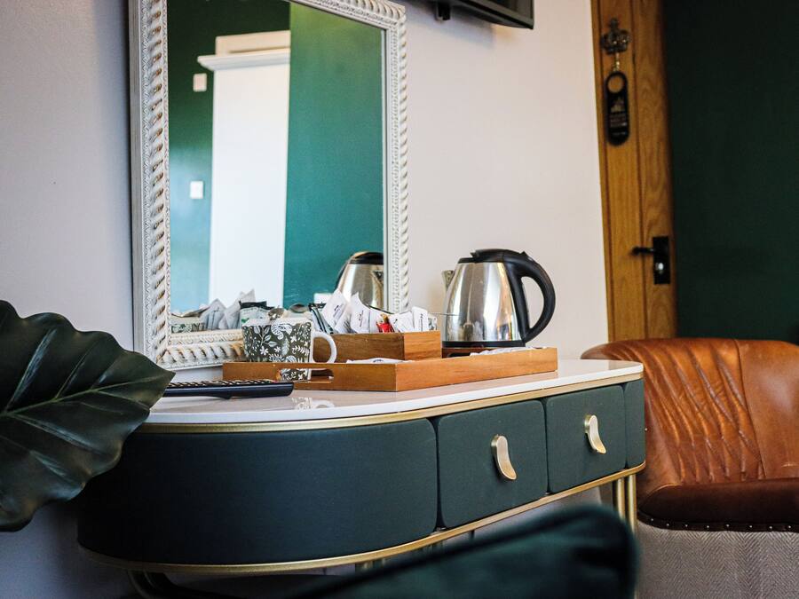 A room with a dark green wall, a white-framed mirror, a wooden cabinet with drawers, a brown leather chair, and a radiator.