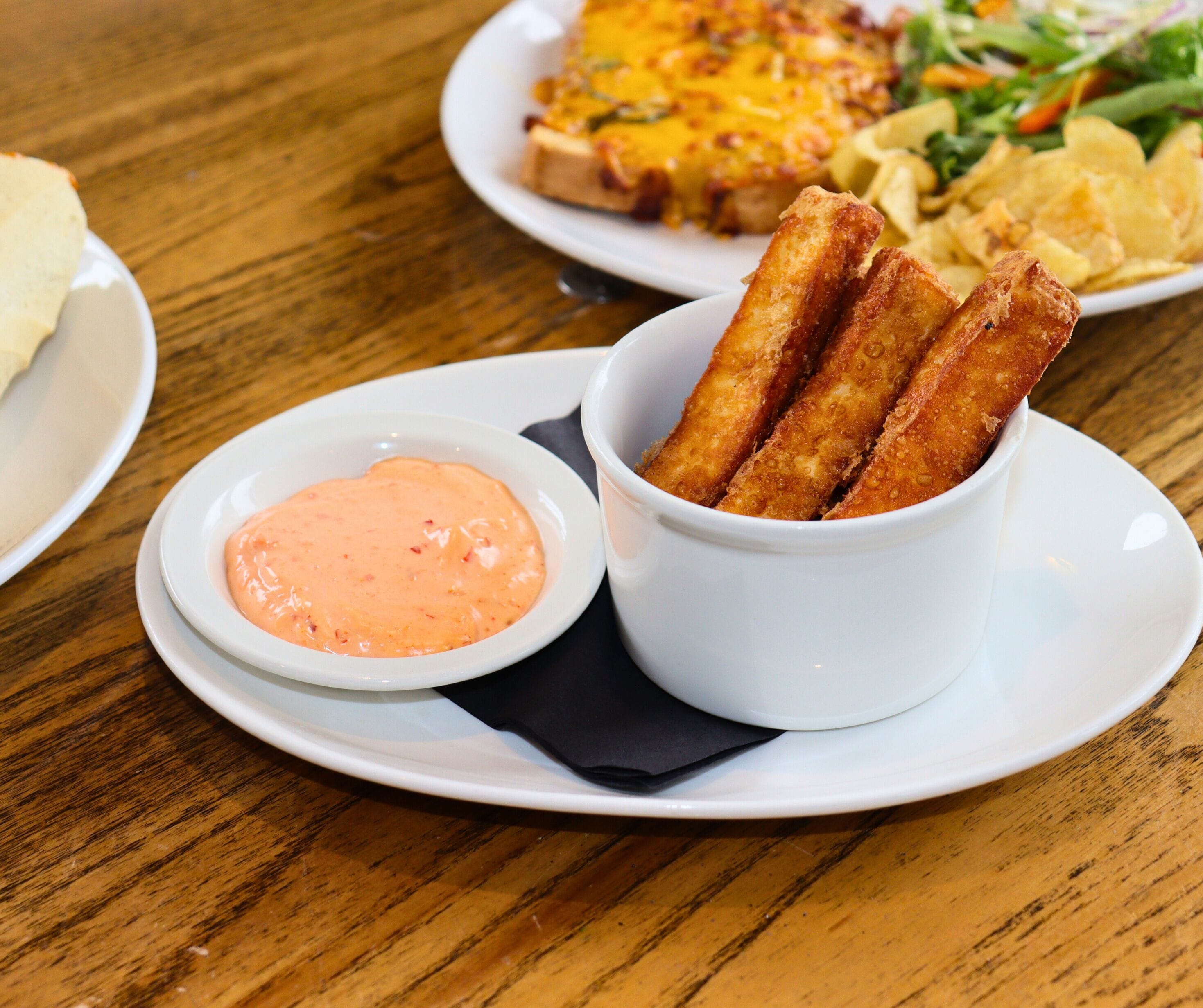 Un plato con tres alimentos fritos y un recipiente pequeño con salsa.