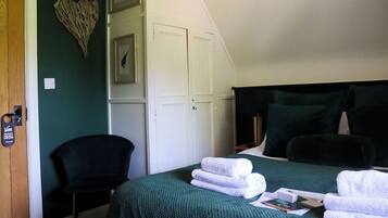 Un dormitorio con cama, ropa de cama verde, una silla, un armario y una decoración con forma de corazón en la pared.
