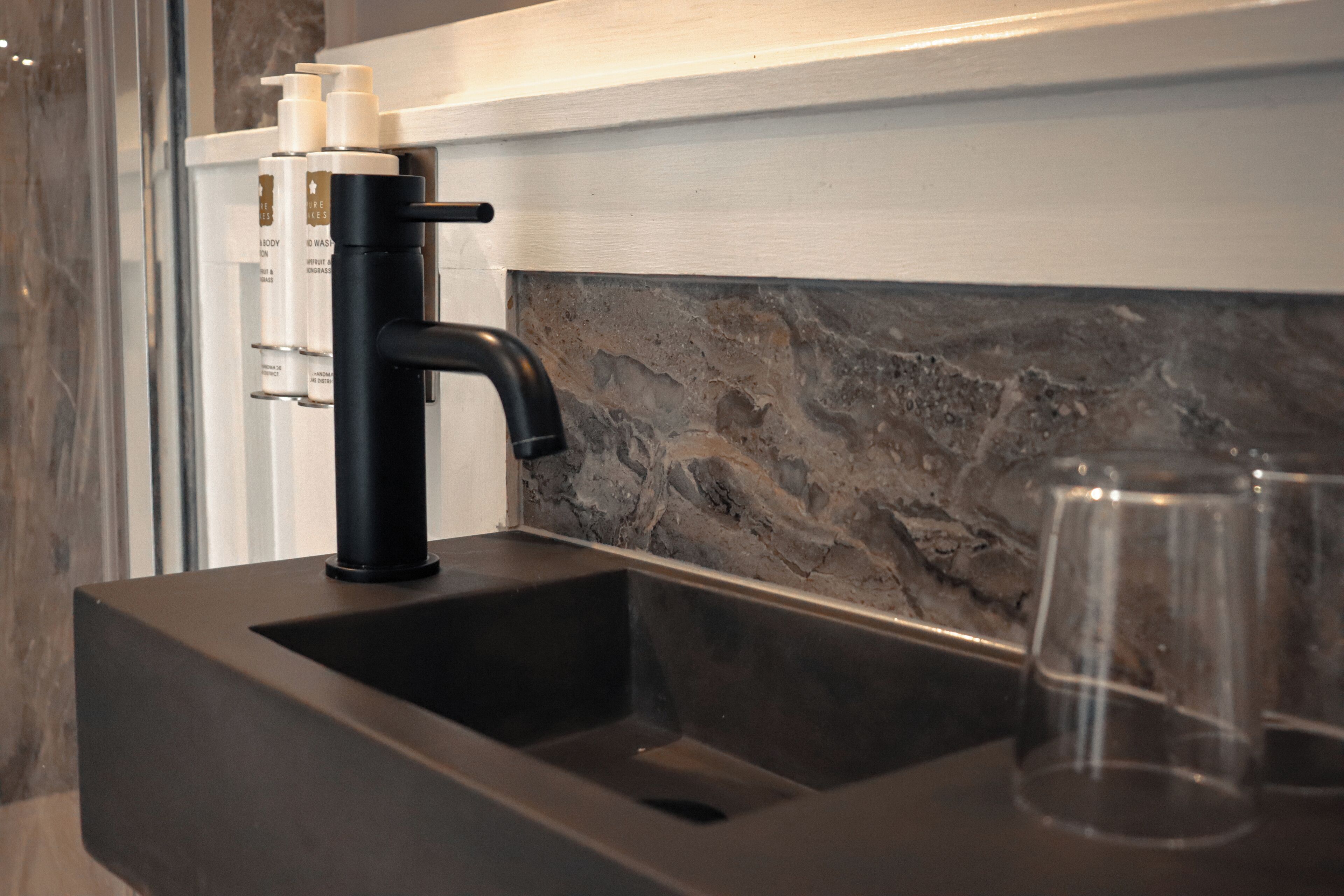 A bathroom with a black sink, a marble backsplash, and a white wall.