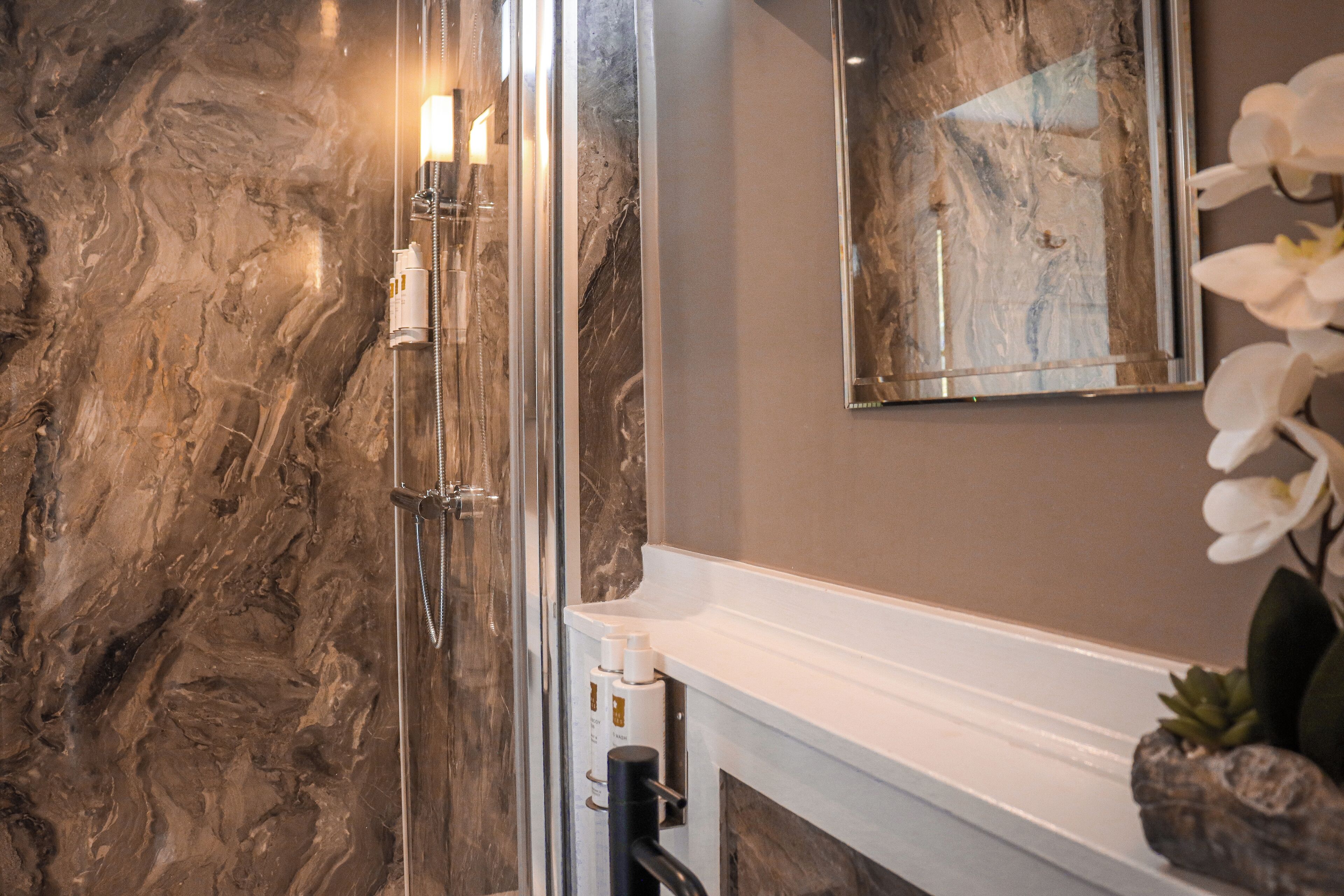 Een badkamer met een marmeren wand, een spiegel, een wastafel en een douche.