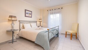 A bedroom with a bed, two bedside lamps, a chair, a window with curtains, and a picture on the wall.