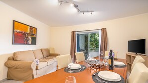 A dining area with a wooden table set for four, a sofa, and a TV on the right.