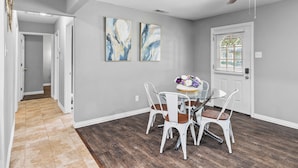 A dining area with a glass table and white chairs, a ceiling fan, and two abstract paintings on the wall. - CASA Noa Noa (Euless)