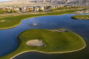 Ein Golfplatz mit einem großen Teich, Sandbunkern und Gebäuden im Hintergrund.