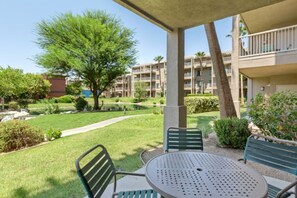 A covered outdoor seating area with a table and chairs, a pathway, and a building with balconies in the background. - WorldMark Indio, 2 Bedroom/2 Bath Condo for Coachella (Indio)