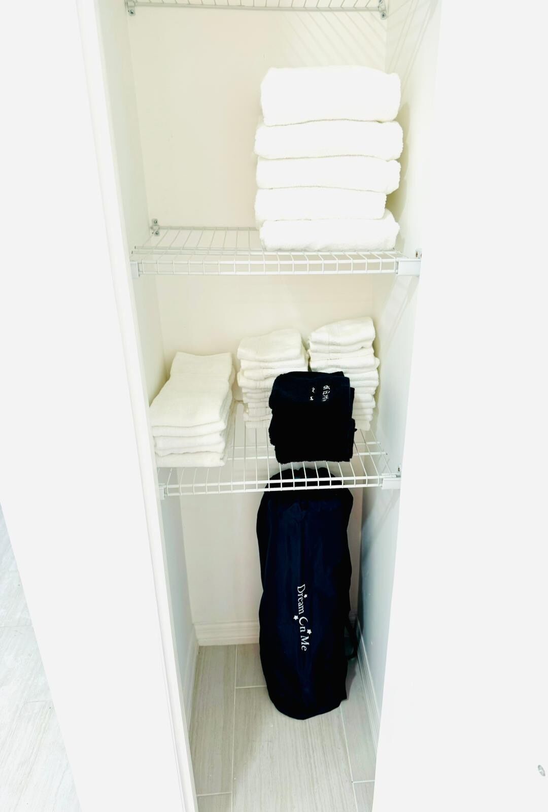 A small walk-in closet with shelves holding folded towels and a black garment hanging on a rack.