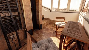 Ein geräumiger Balkon mit Holztisch und -stühlen, einem gemusterten Sofa und Blick auf die Stadt durch große Fenster.