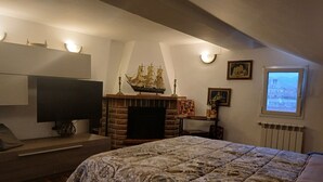 Ein Schlafzimmer mit einem großen Bett, einem Kamin, einem Fernseher und einem Fenster mit Blick auf Gebäude.