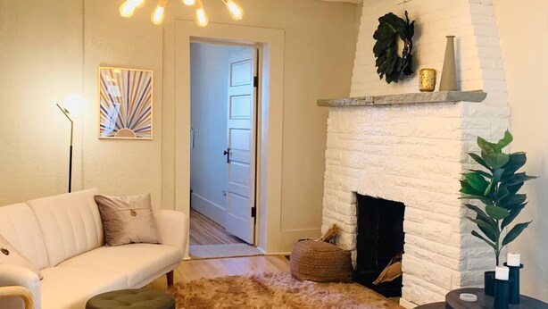 A living room with a white fireplace, a modern chandelier, a sofa, and a wooden floor. - The Roundhouse Charming 4BR House w/ Jacuzzi Tub, WiFi and AC in Central Pueblo (Pueblo)