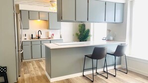A modern kitchen with grey cabinets, a central island, and two bar stools. - The Roundhouse Charming 4BR House w/ Jacuzzi Tub, WiFi and AC in Central Pueblo (Pueblo)