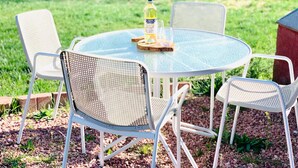 A round glass table with four white metal chairs, a bottle of water, and two glasses on a wooden coaster. - The Roundhouse Charming 4BR House w/ Jacuzzi Tub, WiFi and AC in Central Pueblo (Pueblo)