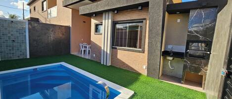 Et moderne hus med to etager, en swimmingpool, grillområde og en lille terrasse med stole.