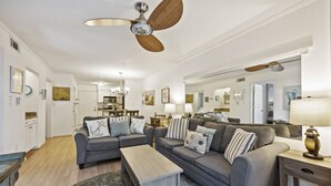 Un salon spacieux avec deux canapés gris, une table basse en bois et un ventilateur de plafond.