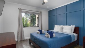 A bedroom with a bed, a window with curtains, a ceiling fan, and a view of greenery outside.