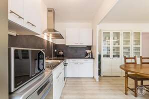 A modern kitchen with stainless steel appliances, white cabinetry, and a dining area with a wooden table and chairs. - 5 BEDROOM GITE WITH LAND IN A SEASIDE VILLAGE WITH ALL SHOPS (Port-Bail-sur-Mer)