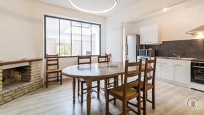 Una cocina moderna con armarios blancos, horno empotrado y microondas. Hay una zona de comedor con una mesa redonda de madera y sillas, además de una chimenea de piedra.