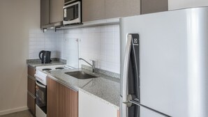 Moderni keittiö, jossa on ruostumattomasta teräksestä valmistettu jääkaappi, mikroaaltouuni, vedenkeitin ja pesuallas.