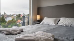 Hotellihuone, jossa on sänky, tyynyjä, yöpöytälamppu ja näkymä kaupunkiin.