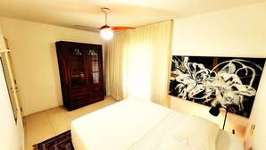 A bedroom with a bed, a wardrobe, a ceiling fan, and a large abstract painting on the wall. - Floripa, small and sexy. (Centro Florianópolis)