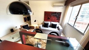 A modern living room with a glass table, two sofas, a large abstract painting, and a view of the city through large windows. - Floripa, small and sexy. (Centro Florianópolis)