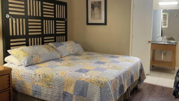 A bedroom with a bed, a headboard, a bedside table, a mirror, and a framed picture on the wall. - Tri-City Motel by OYO Forrest City Spindale (Spindale)