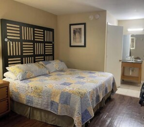 A bedroom with a bed, a headboard, a bedside table, a mirror, and a framed picture on the wall. - Tri-City Motel by OYO Forrest City Spindale (Spindale)