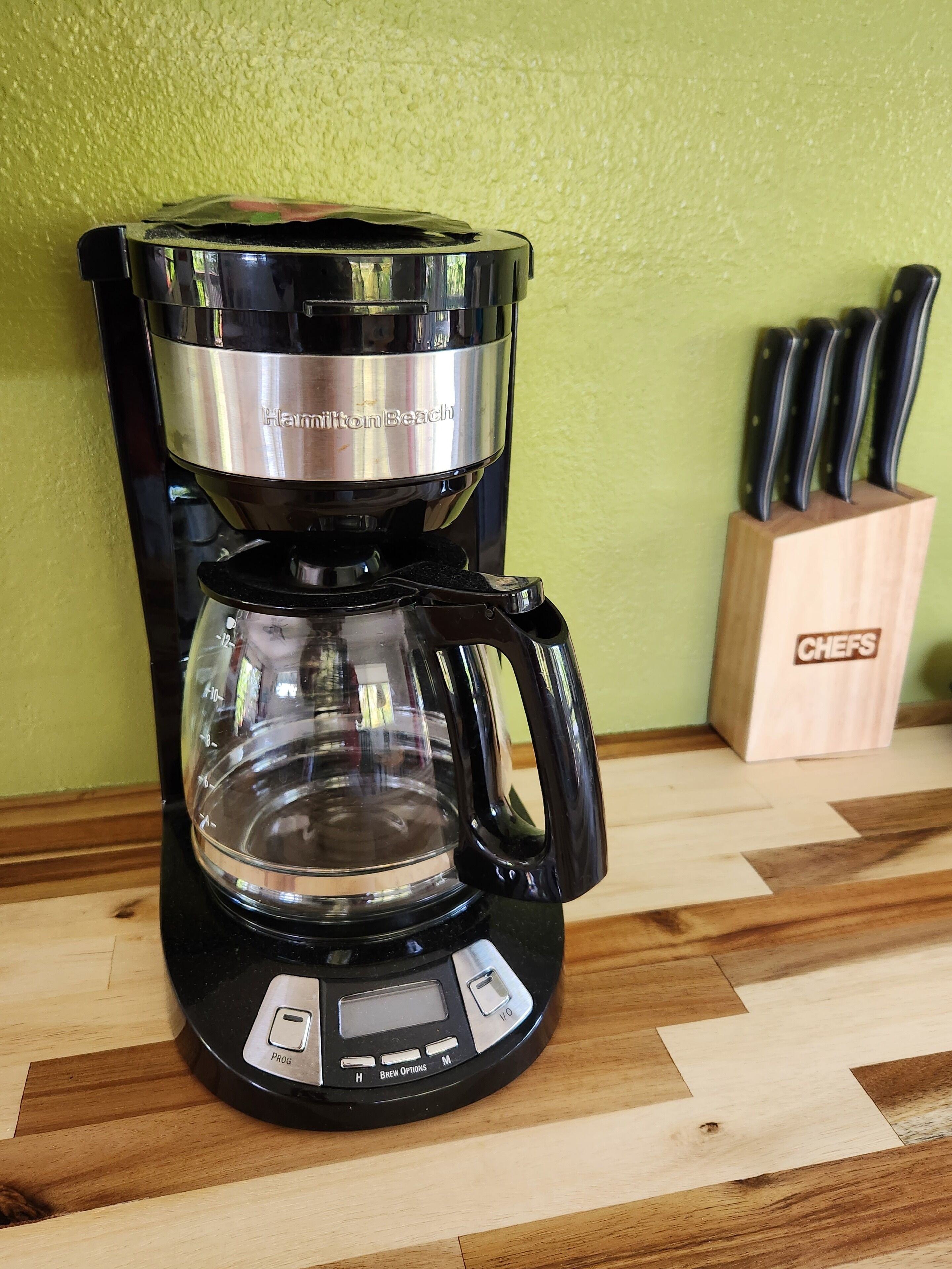 Une machine à café de la marque Hamilton Beach posée sur un plan de travail en bois.