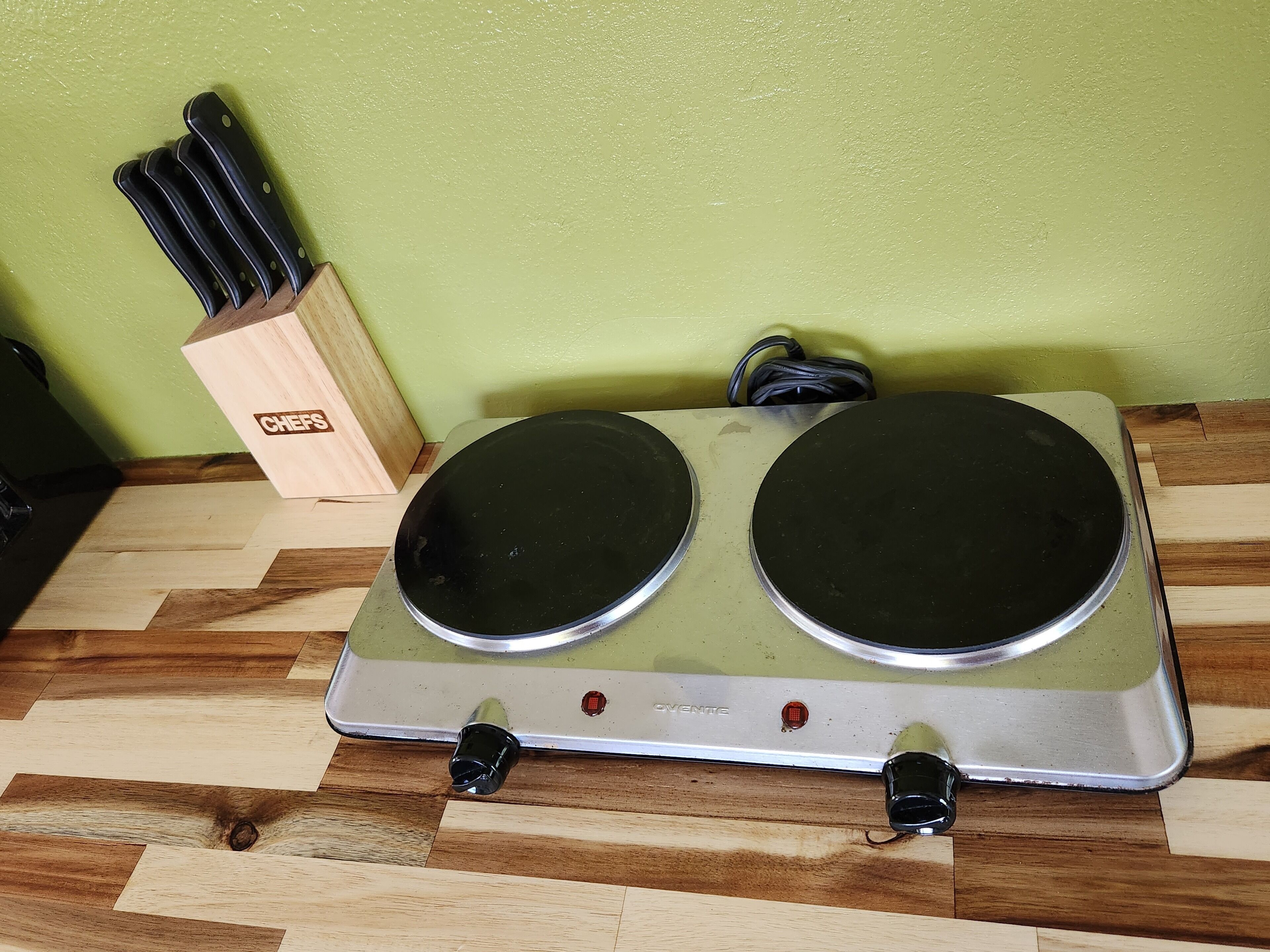 Una cocina con estufa eléctrica doble, un bloque de cuchillos y una pared verde.