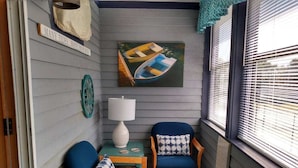 A cozy corner with two blue chairs, a small table, a lamp, and a painting of boats.