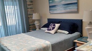 A bedroom with a bed, a nightstand, a lamp, a painting, and a window with curtains.