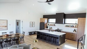 A modern kitchen with a central island, bar stools, and a dining area with a wooden table and chairs.