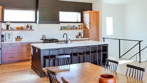 A modern kitchen with a central island, bar stools, and a dining table.