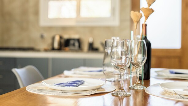 A dining table set with plates, glasses, and a bottle, with a kitchen in the background. -  Apartments Bariloche - San Martin de los Andes Cabins   (San Martín de los Andes)