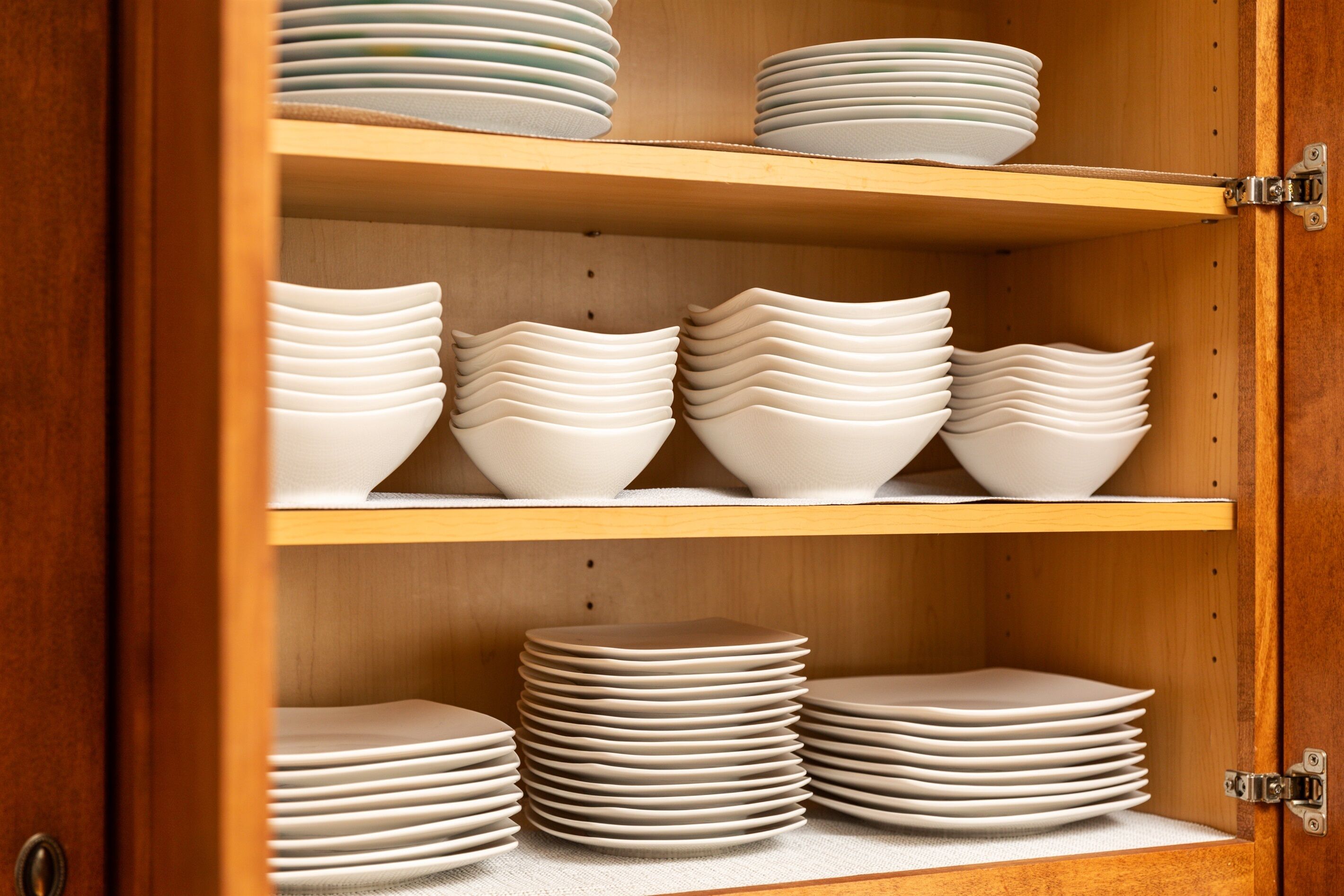 A wooden cabinet with multiple shelves holding stacks of white plates and bowls.