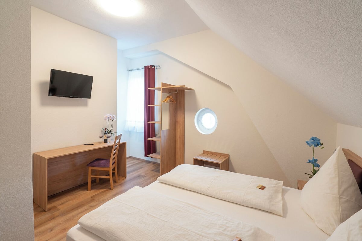 A bedroom with a desk, chair, bed, and a TV on the wall.