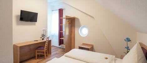 A bedroom with a desk, chair, bed, and a TV on the wall.