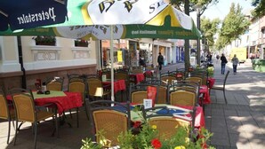Mesa y sillas en terraza, algunas cubiertas por sombrillas, con una calle al fondo.