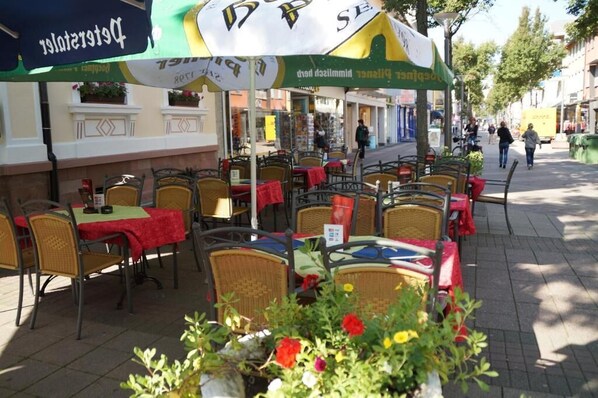 Outdoor seating with tables and chairs, some covered by umbrellas, and a street in the background. - Hotel Schwert (Kehl)