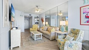 Un salon comprenant un canapé, des fauteuils, une table basse et un téléviseur. On y trouve également un ventilateur de plafond, un miroir et un tapis sur le sol.