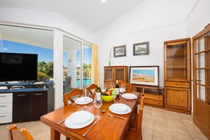 Un coin repas avec une table dressée pour quatre personnes, un téléviseur et une vue sur l’extérieur.