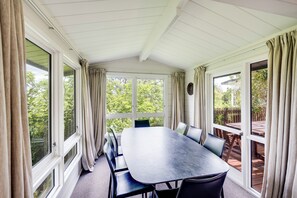 Een overdekt terras met een tafel en stoelen, grote ramen en uitzicht op de omgeving.