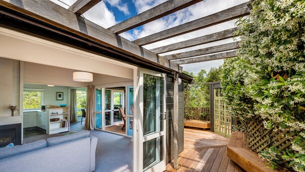 Ein modernes Haus mit einer Holzterrasse, einer Glastür, die auf eine Terrasse führt, und Blick auf einen Garten.