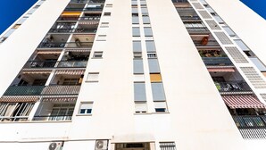 Un edificio alto con varios balcones, unidades de aire acondicionado y una entrada visible.